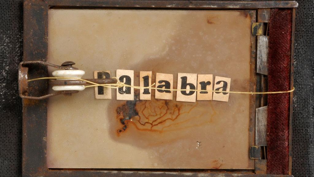 Fotografía de una especie de antigua trampa para ratones, con trozos de papel  en los que se deletrea "palabra"