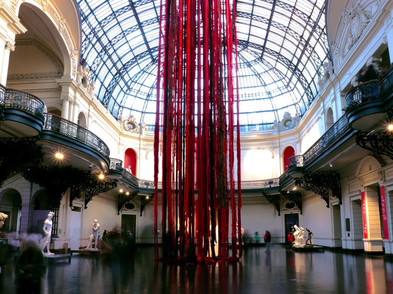 Fotografía del hall del Museo con instalación colgante hecha con lanas rojas