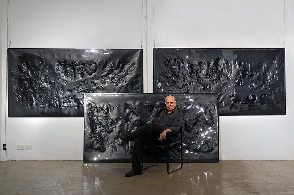 Hombre sentado junto a tres cuadros negros con figuras en relieve