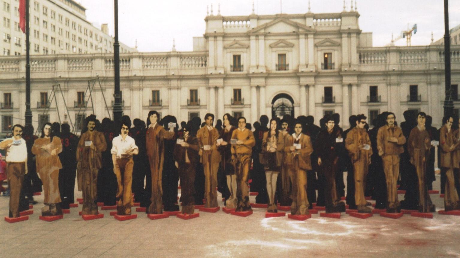 Fotografía de figuras de personas situadas frente a La Moneda