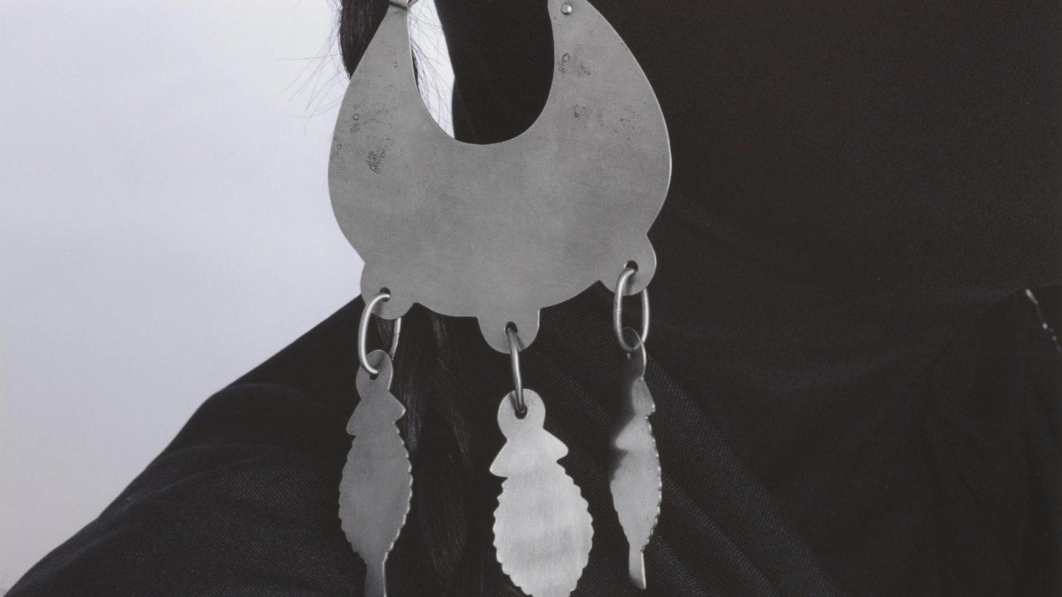 Silueta negra utilizando un arete de platería mapuche