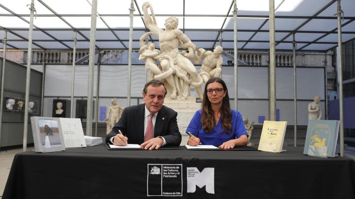 Fotografía de un hombre y una mujer sentados frente a un mesón, firmando documentos