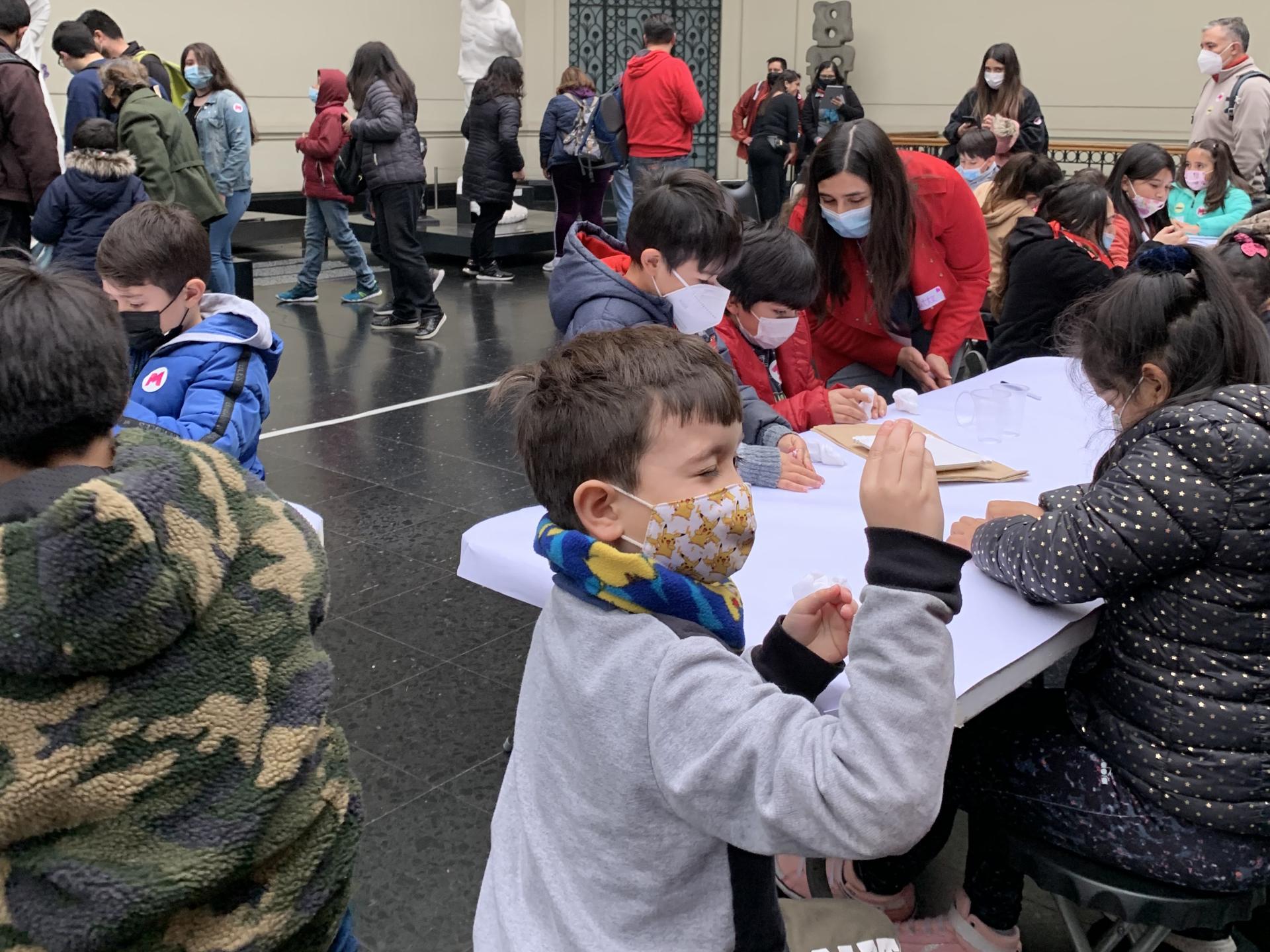 Grupo de niños sentados frente a mesas en el hall del Museo