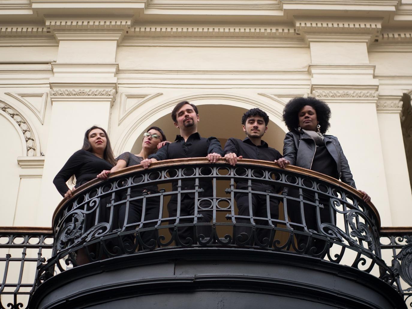 Imagen de tres mujeres y dos hombres vestidos de negro, mirando hacia abajo desde un balcón