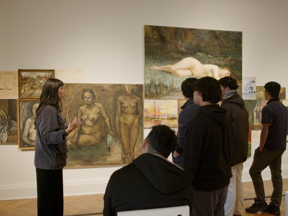 Fotografía de una joven conversando con estudiantes en una sala de exposición