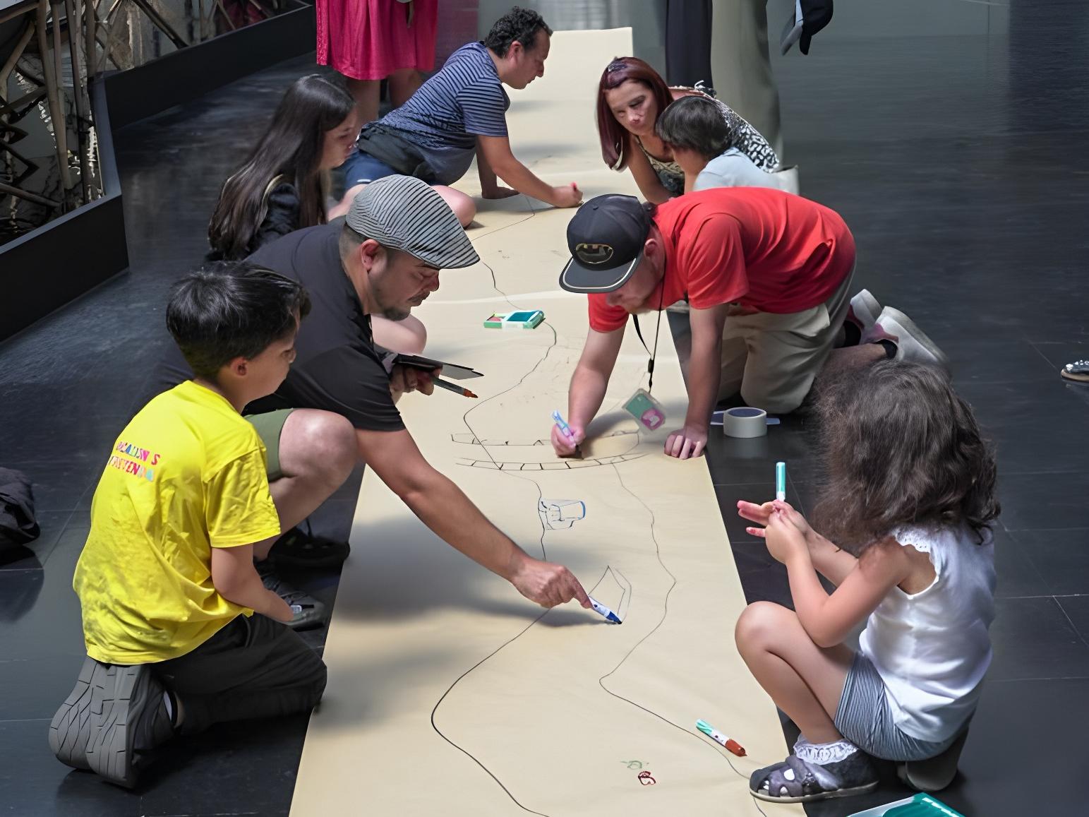 Personas sentadas en el piso del hall, dibujando sobre un pliego de papel