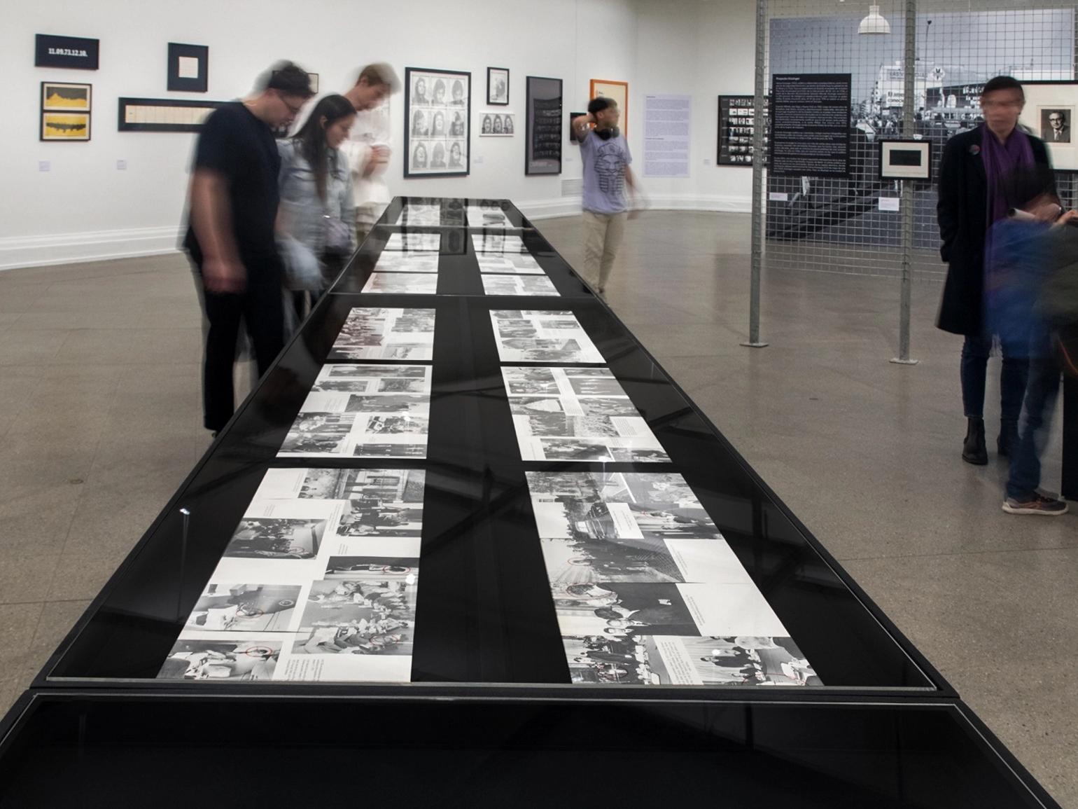 Fotografía de personas en una exposición, mirando un mesón con imágenes