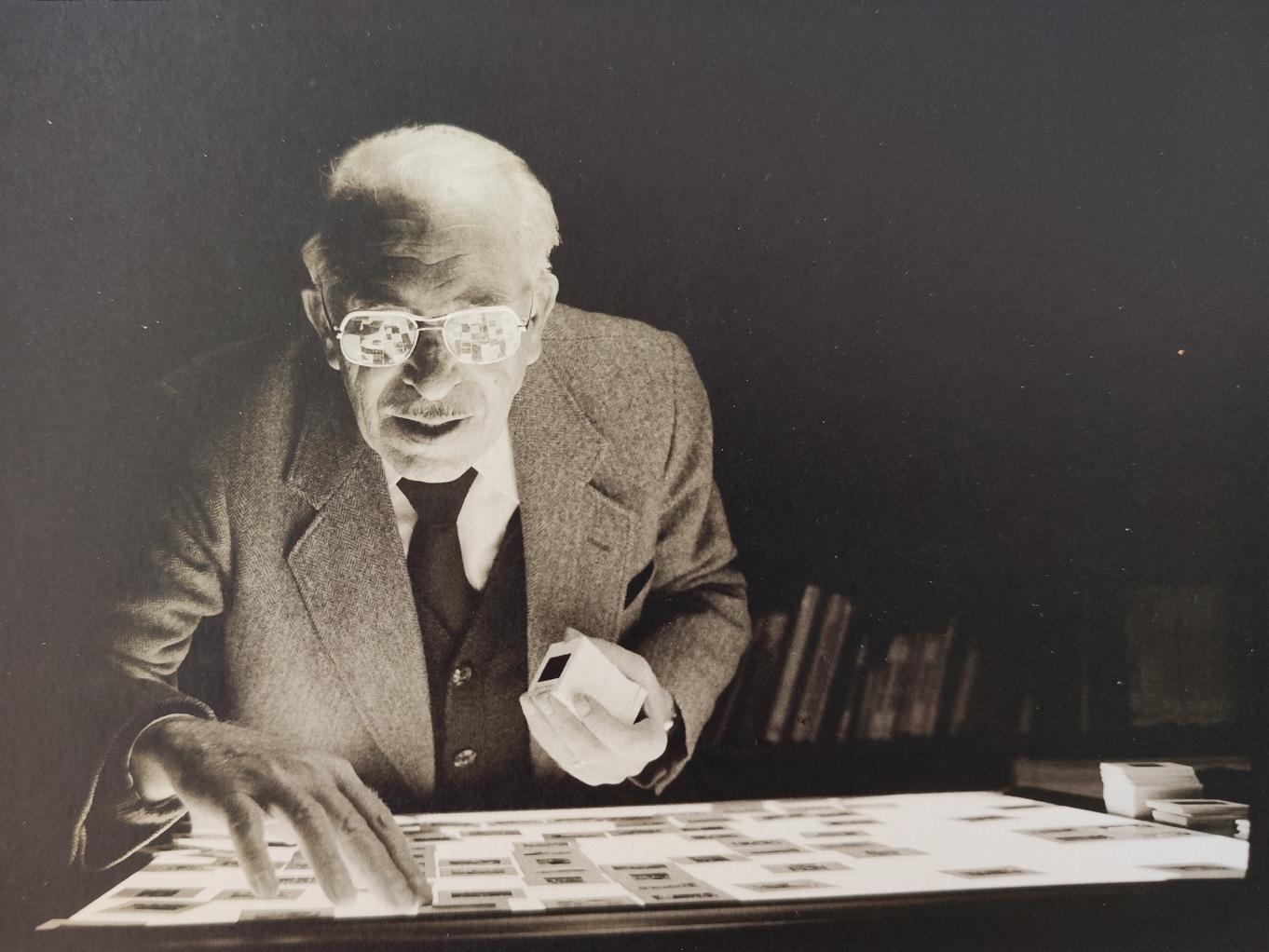 Fotografía en blanco y negro de un hombre mayor con traje, trabajando con negativos de fotografías