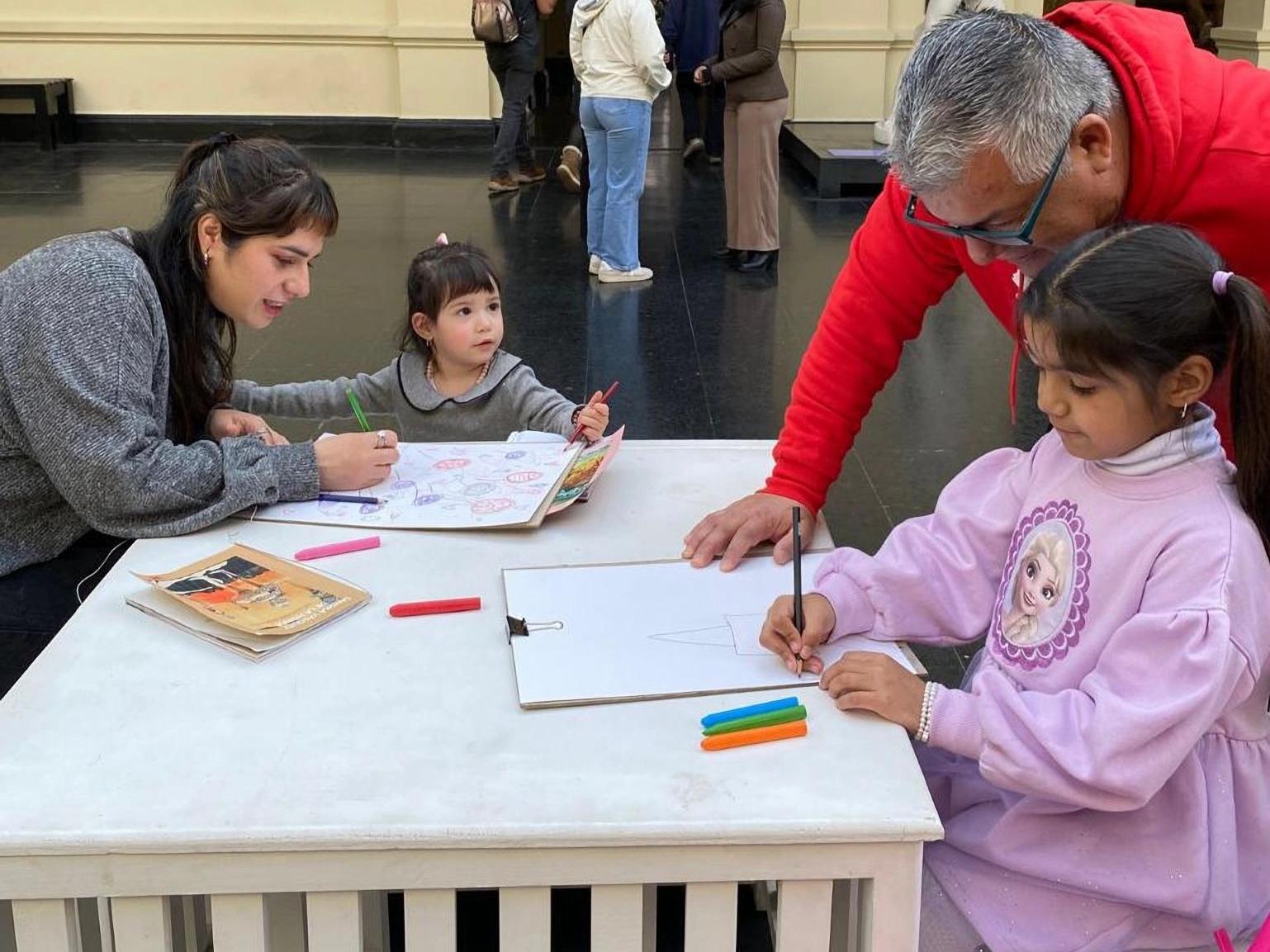Fotografía de niñas dibujando, acompañadas de adultos