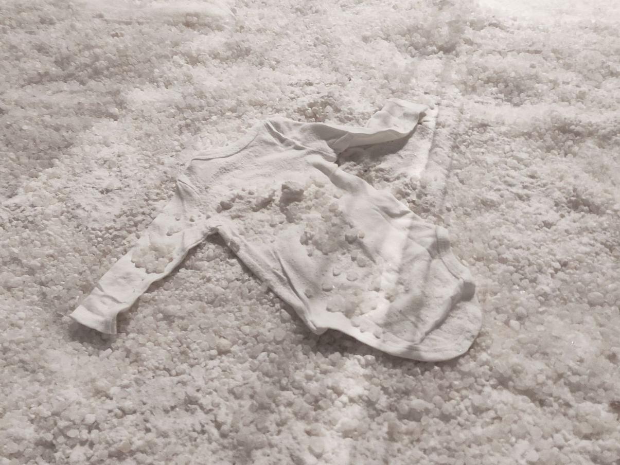 Fotografía de una prenda de ropa de bebé de color blanco, cubierta de sal
