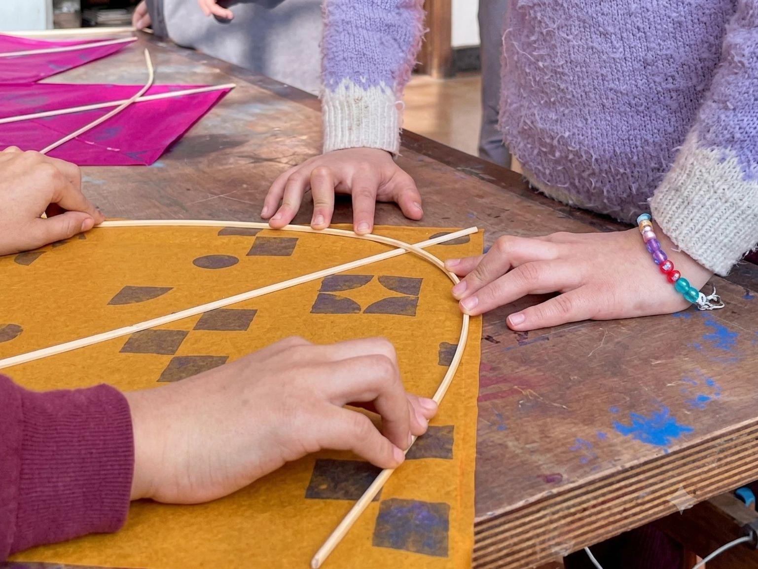 Fotografía de las manos de dos personas creando un volantín.