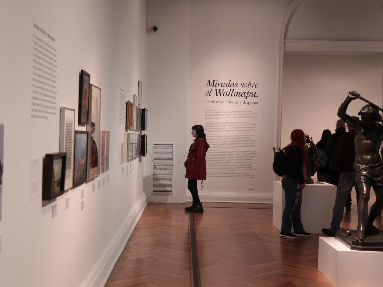 Una mujer con una chaqueta larga de color burdeo mirando la exposición