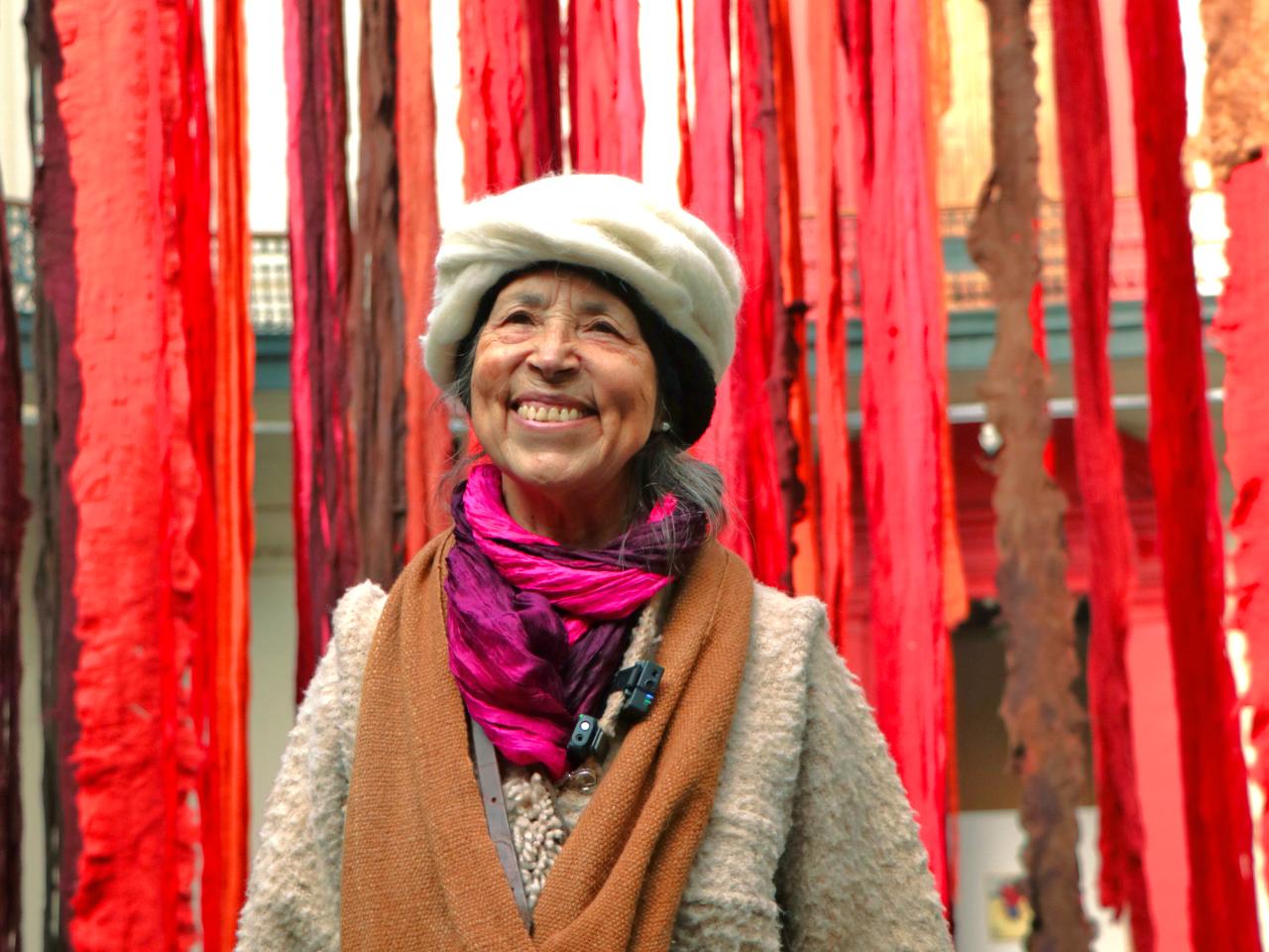 Una mujer mayor sonriendo con telas rojas colgando detrás de ella