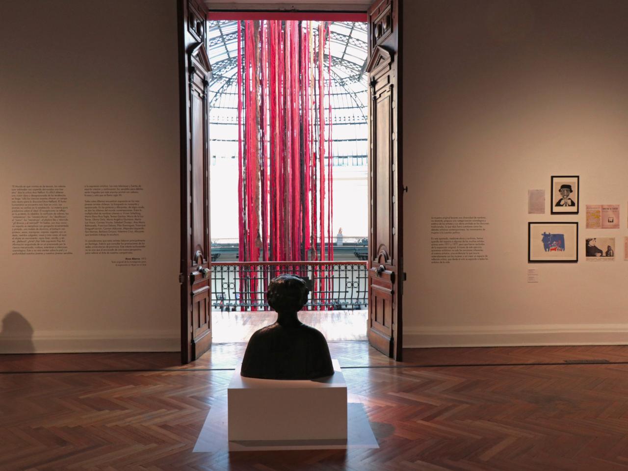 Se observa una escultura en medio de la sala y fuera de esta se encuentran telas colgando de colores rojo y café