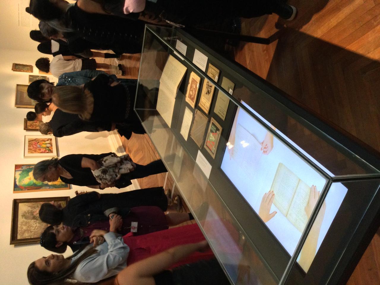 Personas en la sala de exposición, en medio se encuentra una vitrina con documentos