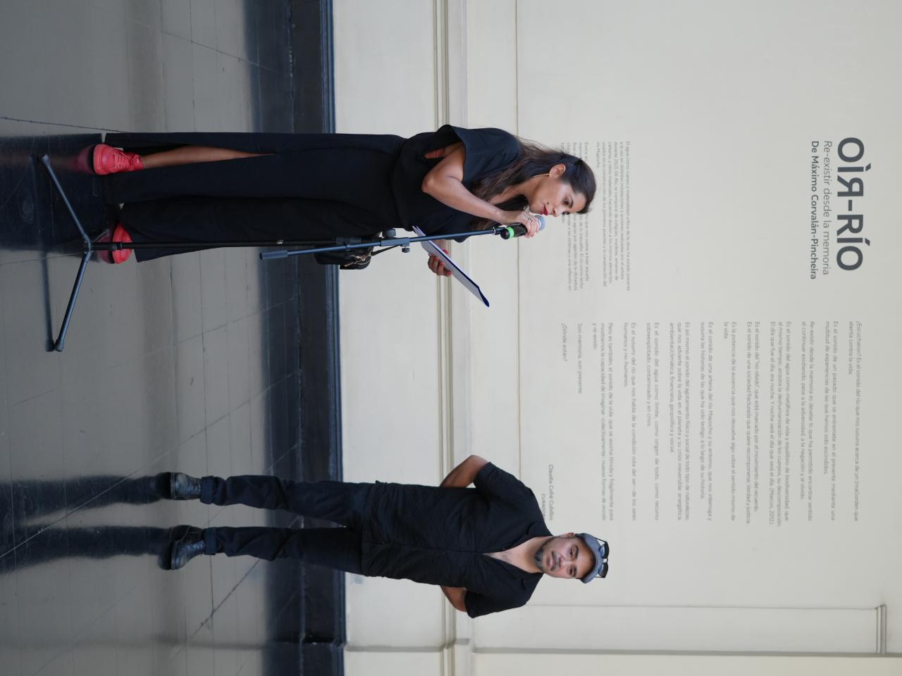 Una mujer hablando por un micrófono y el autor al lado de ella