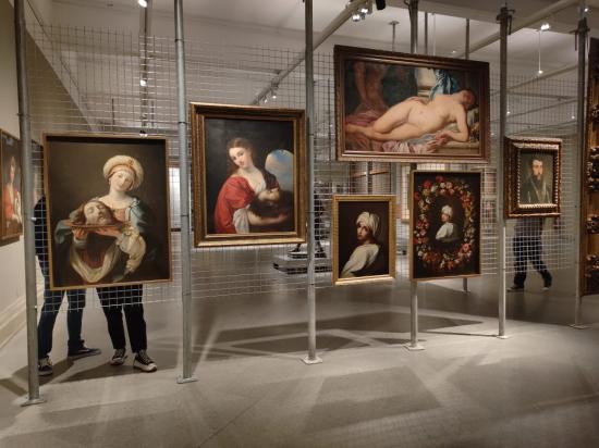 Exposición con pinturas colgadas de una rejilla