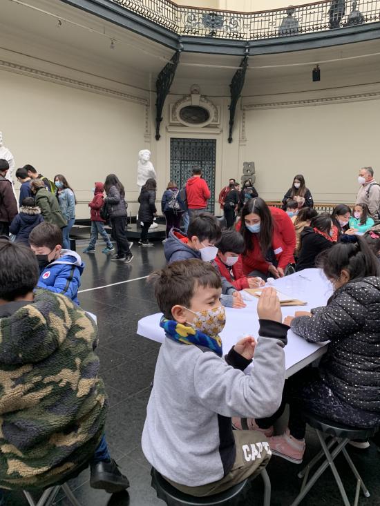 Grupo de niños sentados frente a mesas en el hall del Museo