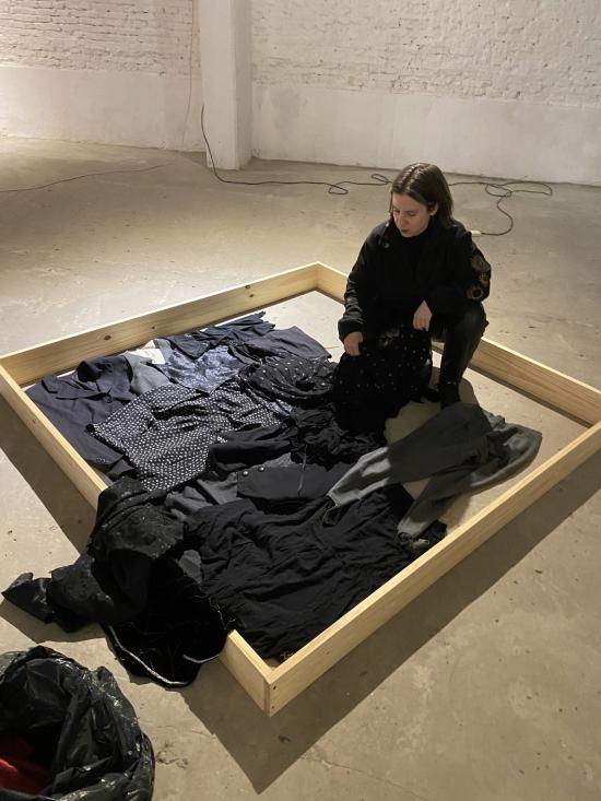 Fotografía de mujer junto a varias prendas de vestir negras, dispuestas en el suelo