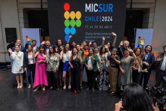 Grupo de personas saludando con las manos en alto, frente a un cartel con el texto "MICSUR Chile 2024"