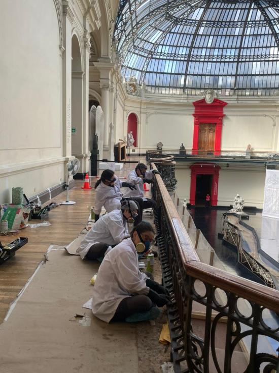 Grupo de personas con bata blanca y mascarillas, arreglando barandas metálicas en el museo