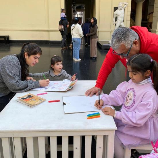 Fotografía de dos niñas dibujando, acompañadas de adultos