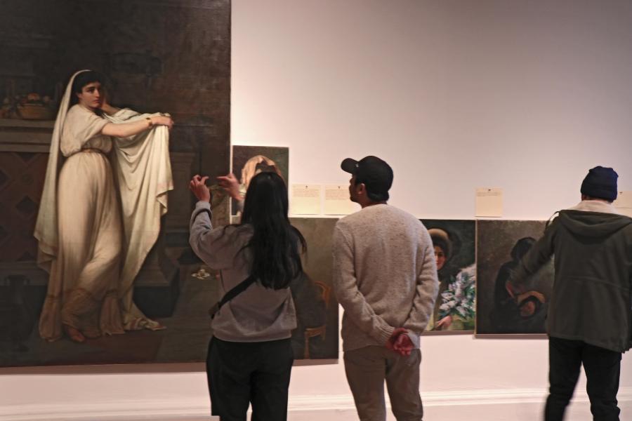 Una mujer y un hombre mirando un cuadro de una mujer con vestido blanco