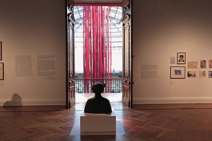 Se observa una escultura en medio de la sala y fuera de esta se encuentran telas colgando de colores rojo y café