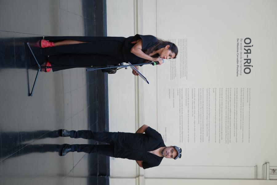 Una mujer hablando por un micrófono y el autor al lado de ella